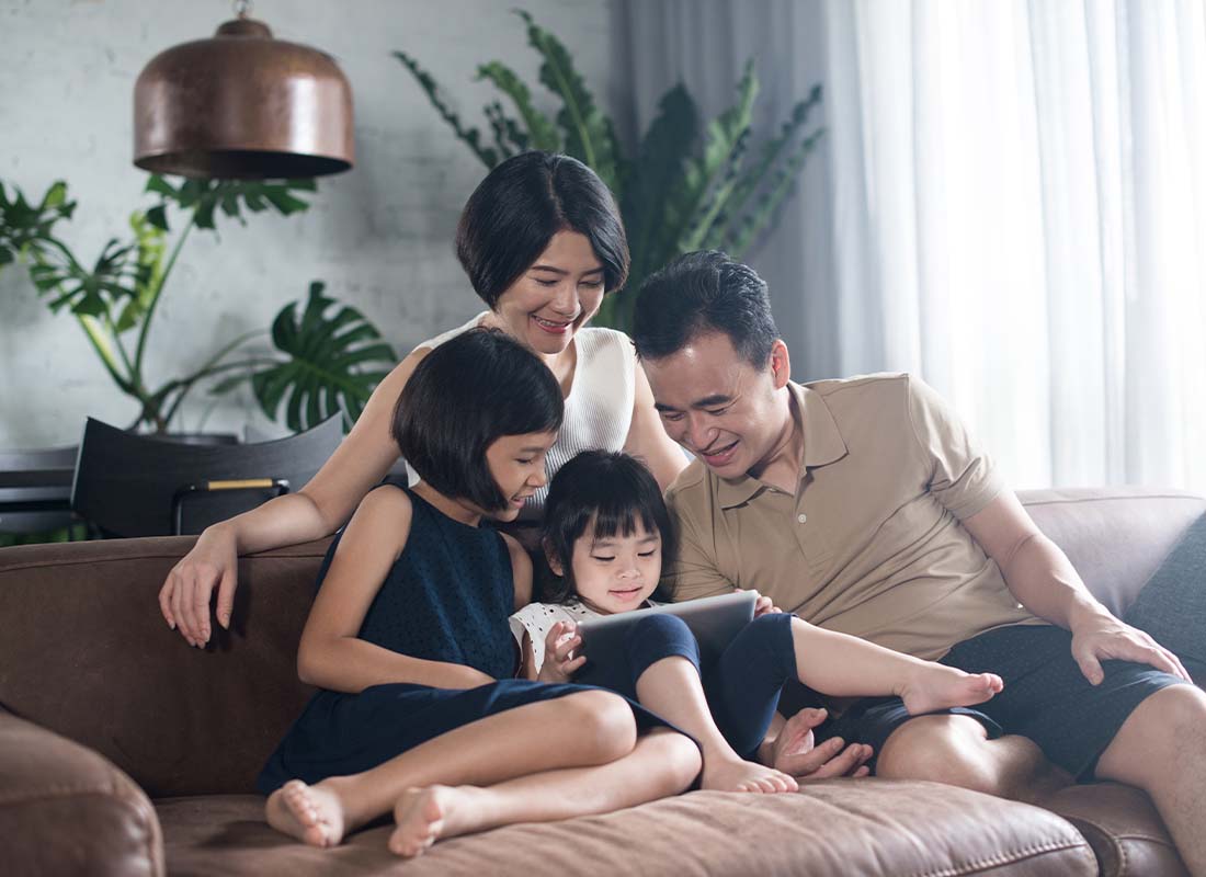 Umbrella Insurance - Happy Family Using a Tablet Together at on the Living Room Sofa of Their Modern Home